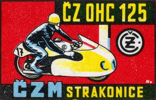 Závodník v modré kombinéze leží na žlutém závodním motocyklu s aerodynamickou kapotáží. Na červeném podkladu vpravo logo ČZ v kruhu.